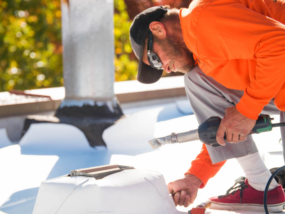 Roofer installing TPO roofing Roofer installs TPO roofing around a pipe support using a hand-held, hot air welder