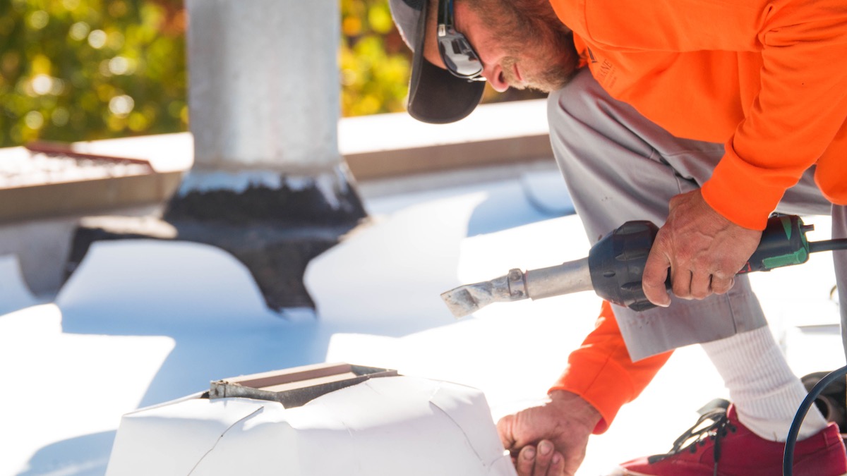 Roofer installing TPO single-ply roofing around a pipe support using a hot air welder